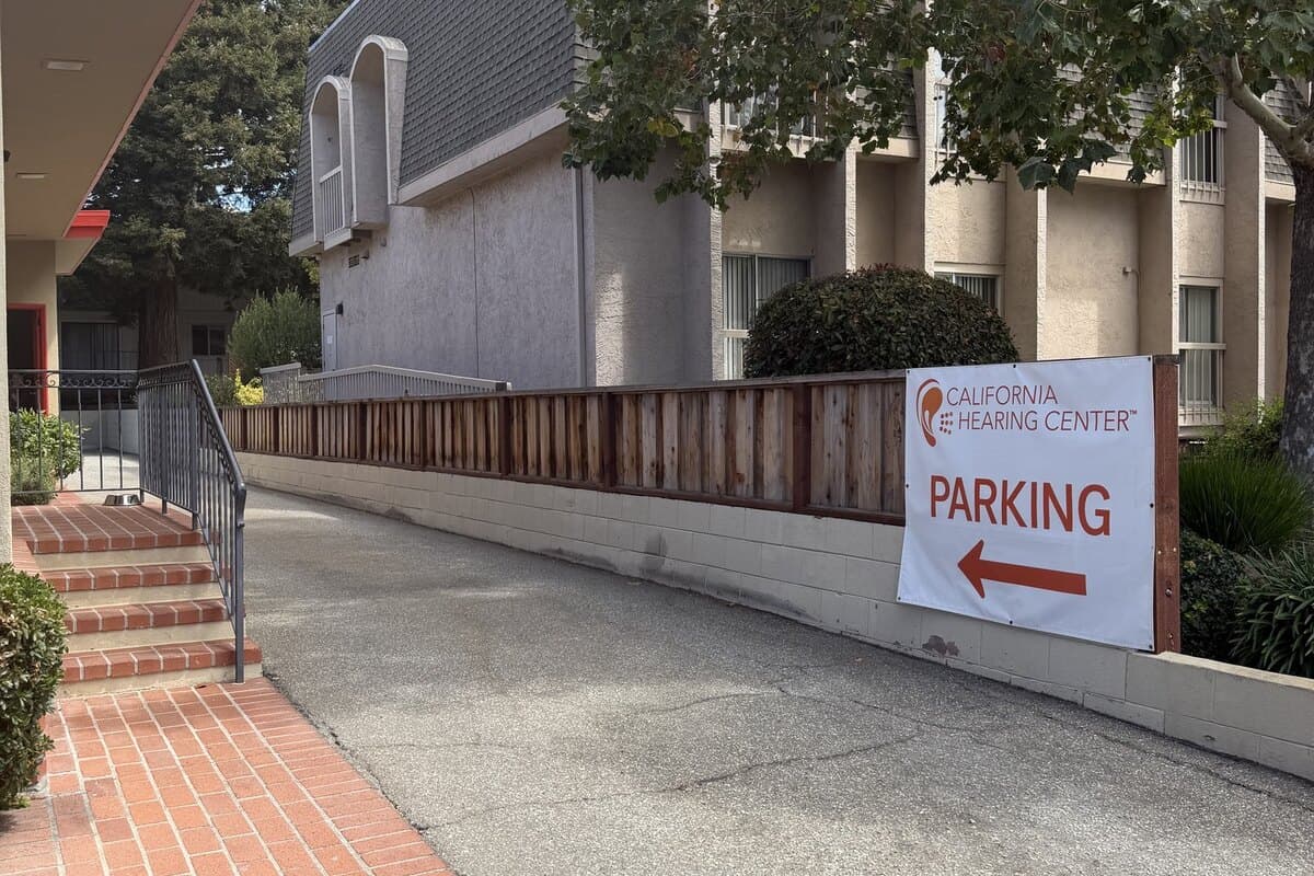 A driveway running alongside the office building, with a banner on the fence reading California Hearing Center Parking and an arrow.